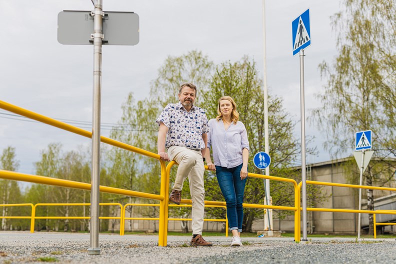 Anssi Hietanen and Eeva Tuomi look at the camera and lean on a fence.